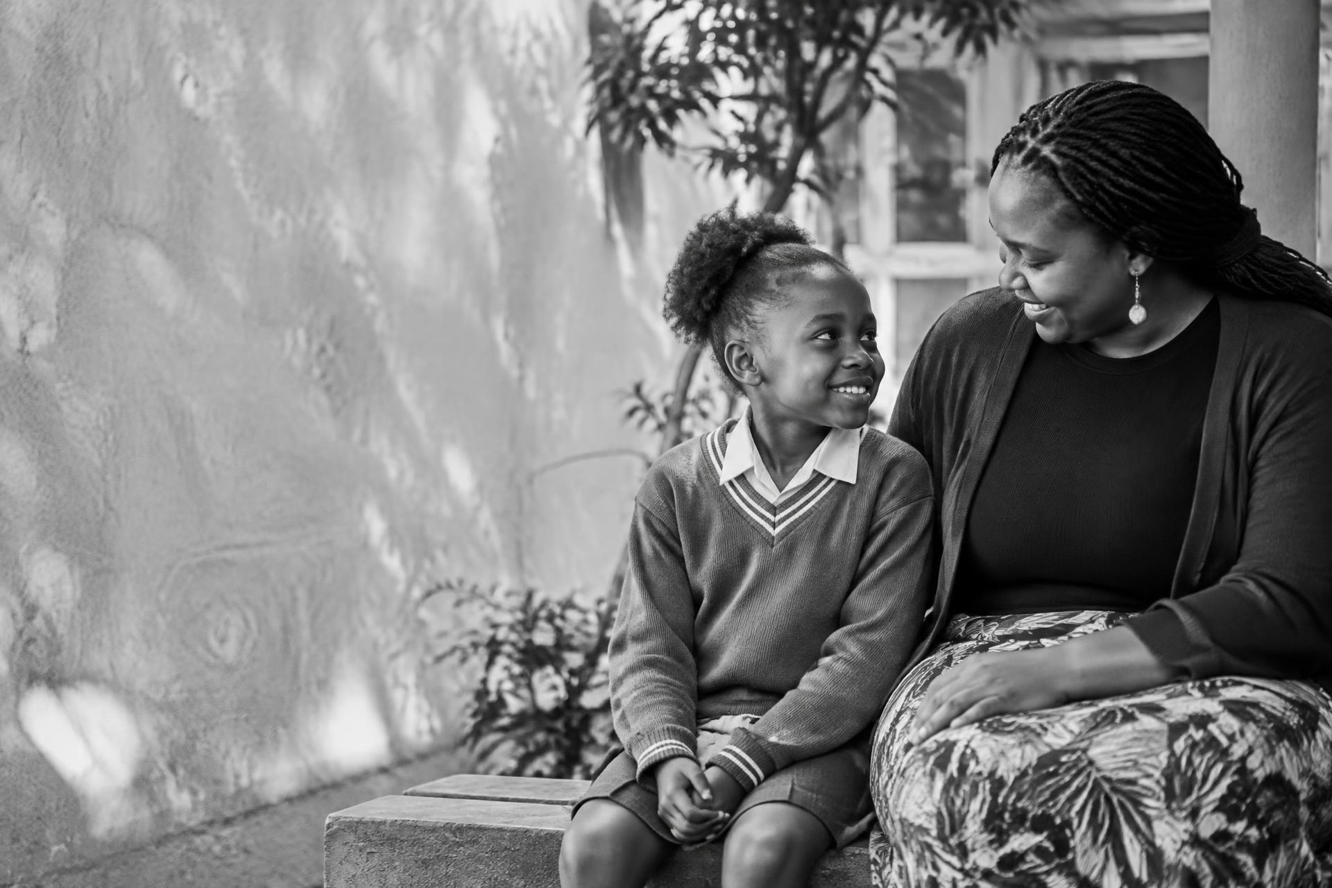 Illustrative editorial photograph of a child and caring adult sharing a warm moment in a courtyard.